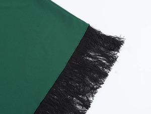 Dettaglio del tessuto verde con rifiniture in frange nere su un abito lungo da vacanza