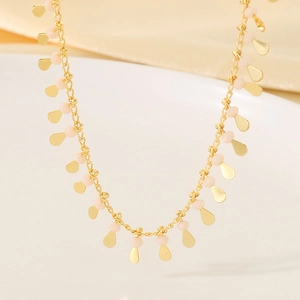 Macro shot of gold necklace with pale pink beads and water drop pendants on ceramic