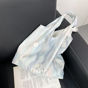 Détail du tote bag en toile aux tons macaron avec broderies de fleurs 3D sur une chaise