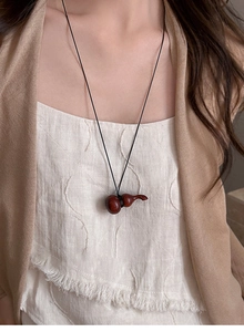 Gros plan d'un pendentif gourde en bois artisanal sur un collier minimaliste noir