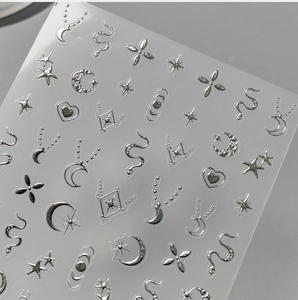 Macro detail of silver metallic nail art stickers featuring moon, star and snake patterns