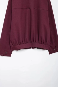 Detail of burgundy twill jacket showing silver zipper and buttoned cuffs on white background