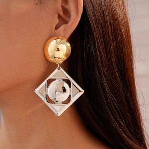 Close-up of geometric gold circle and silver rhombus earrings worn by a model