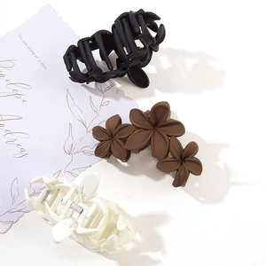 Three matte floral hair claws in black brown and cream on a minimalist background