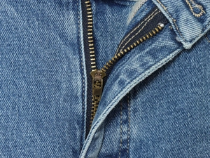 Close-up of durable brass metal zipper and stitching on blue denim wide-leg pants