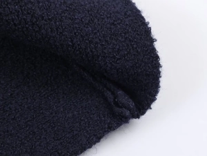 Detailed macro shot of dark blue boucle knit fabric texture for short winter coat