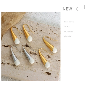 Detail of gold and silver water-drop earrings with milky white resin charms on stone