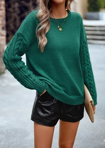 Dettaglio della trama a trecce sulle maniche del maglione verde a maniche lunghe
