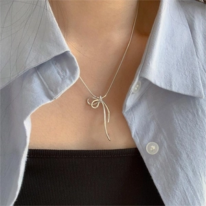 Close-up of a silver bow pendant on a delicate snake chain necklace worn by a model