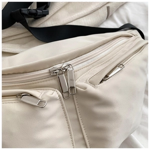 Detail of cream nylon crossbody bag with silver metal zippers and adjustable black strap