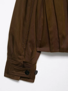 Detail view of dark brown jacket sleeve featuring pleats, twill fabric, and black buttons