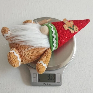 Detailed close-up showing a Christmas gingerbread gnome plush being weighed on a digital scale