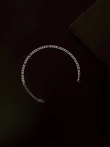 Detailed view of silver Figaro chain bracelet with metallic luster on dark stone background