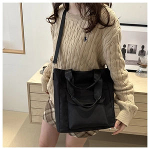 Detail of black nylon tote bag worn on shoulder showing its waterproof texture and strap