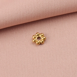 Detailaufnahme goldener Schneeflocken-Metallperlen auf weichem rosa Stoffhintergrund