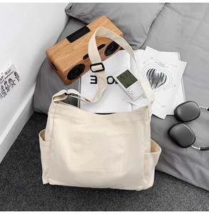 Vue à plat d'un sac bandoulière en toile beige avec de larges bretelles sur un lit