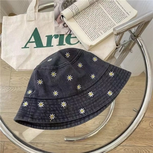 Retro black denim bucket hat with white daisy embroidery on a modern glass side table