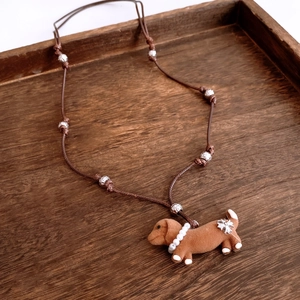 Detail of brown dachshund puppy pendant with pearl collar and silver floral beads