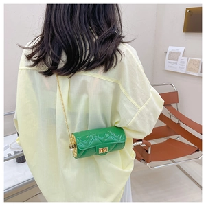 Green cylindrical crossbody bag with gold chain strap shown on model in cafe setting