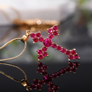 Macro shot of gold cross pendant necklace featuring inlaid ruby red crystal zircons