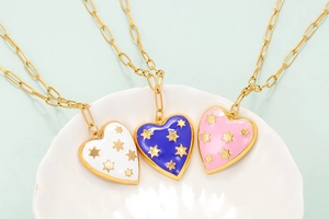 Close-up of heart and star pendant necklaces in blue, pink, and white enamel on a shell tray