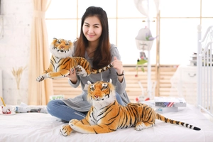Detailed comparison of large and small realistic plush tiger toys held by a model