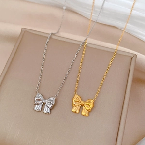 Detailed view of gold and silver bow necklaces on a beige gift box with silk fabric