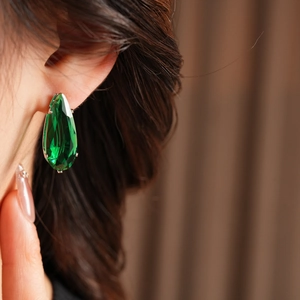 Close-up of green teardrop zircon earrings featuring claw-set gems on a model