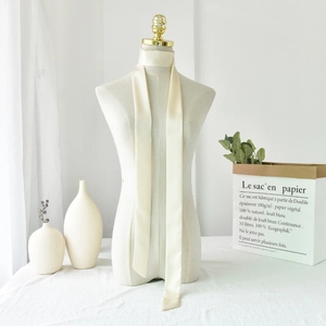 Detail of elegant ivory satin skinny scarf tied as a bow on a white ceramic vase