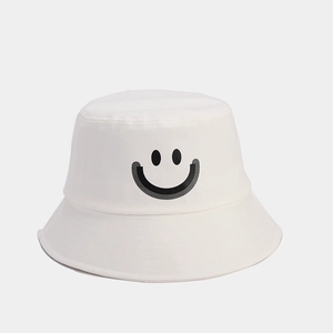 Close-up of white cotton bucket hat featuring a black embroidered smiley face pattern