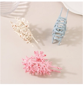 Three spotted claw clips in beige, light blue and pink colors on plain background