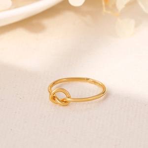 Close-up of golden minimalist knot ring on warm textured background with dried flowers