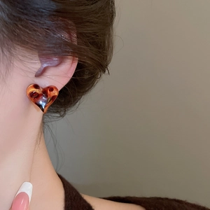 Detail of vintage heart-shaped leopard resin earrings on model with tortoise pattern