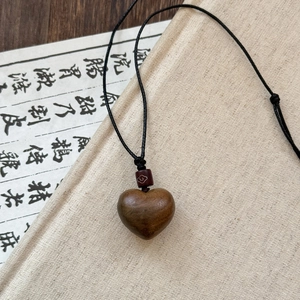 Detail of wooden heart pendant with woven cord and patterned ceramic bead