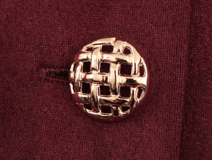 Detailed macro view of a vintage hollow gold metal button on a dark red knitted garment