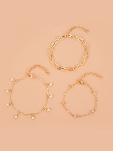 Dettaglio del set di 3 catene dorate con perle e maglie cubane su uno sfondo beige