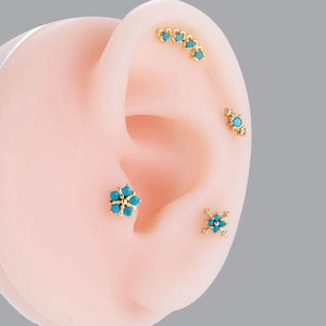 Close-up of gold turquoise stud earrings with flower designs on a silicone ear model