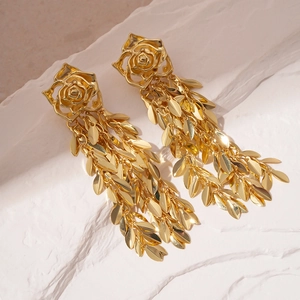 Macro detail of gold rose earrings with long leaf tassels on a white stone base