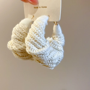 Dettaglio di orecchini a cerchio in lana intrecciata bianco panna per lo stile autunnale