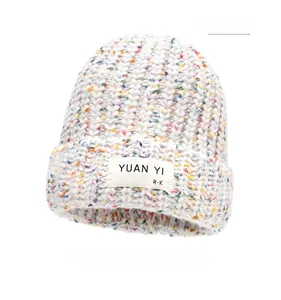 Close-up of beige knitted beanie featuring colorful flecks and a rectangular fabric label