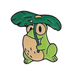 Gros plan du mignon pin's grenouille en émail vert tenant une feuille de lotus