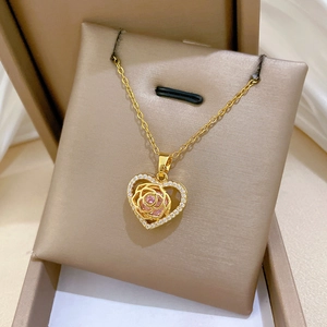 Detail of gold heart pendant with engraved rose and pink gem in a beige gift box