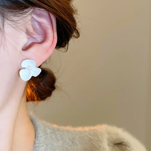 Detailed view of white floral stud earring with a central pearl on model's ear
