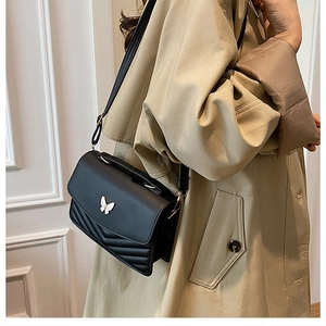 Detail of black V-quilted handbag with silver butterfly buckle on a model's shoulder