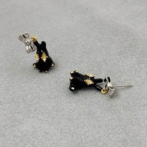 Macro view of black enamel rabbit earrings with silver bow and yellow gemstone inlay