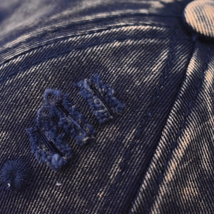 Detailed macro view of distressed denim fabric and vintage embroidery on baseball cap