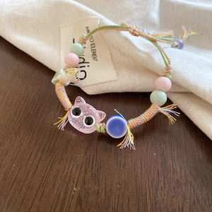 Detail of handmade woven bead bracelet featuring a pink translucent kitten charm on wood