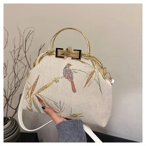 Detail of bird and bamboo embroidery on a beige vintage style handbag with metal handle