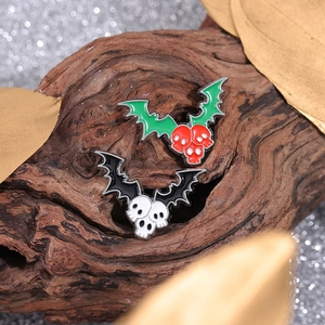Gothic bat wing skull enamel pins on wood display with festive golden leaves and bokeh
