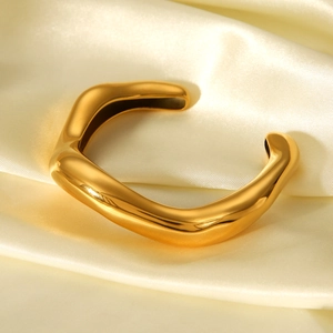Macro shot of gold irregular wave cuff bracelet on elegant cream satin fabric
